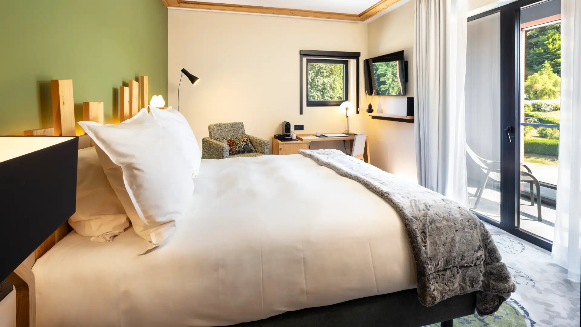 Chambre avec un lit double, une table de chevet, un bureau, des fenêtres avec vue sur l'extérieur et une porte vitrée donnant sur un balcon