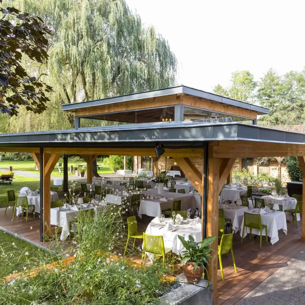 Une terrasse couverte en bois avec des tables dressées pour un repas, entourée d'arbres et de verdure
