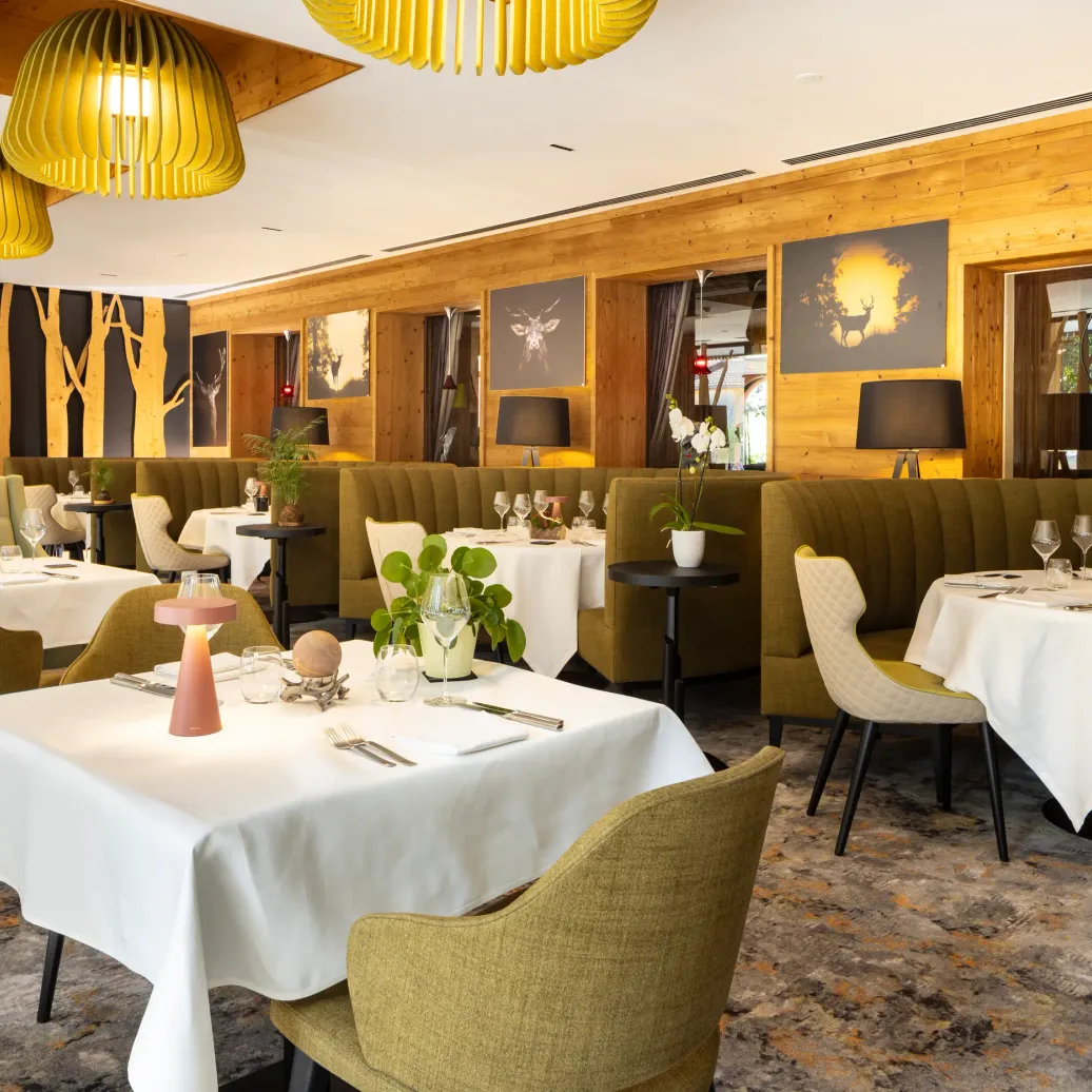 Restaurant élégant avec des tables dressées, des chaises vertes, des luminaires jaunes et des murs en bois