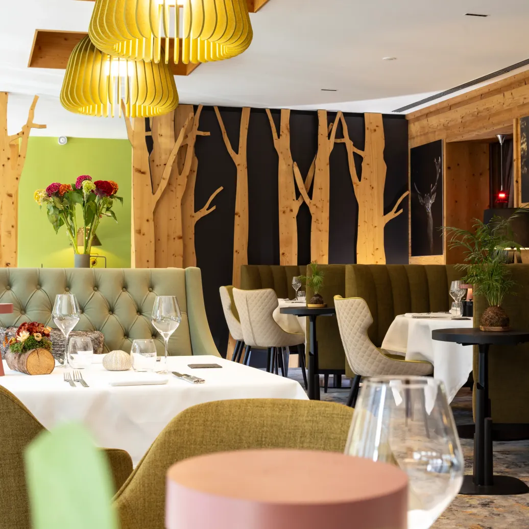 Restaurant élégant avec des tables dressées, des banquettes vertes et des suspensions lumineuses dorées, des murs en bois et des plantes décoratives