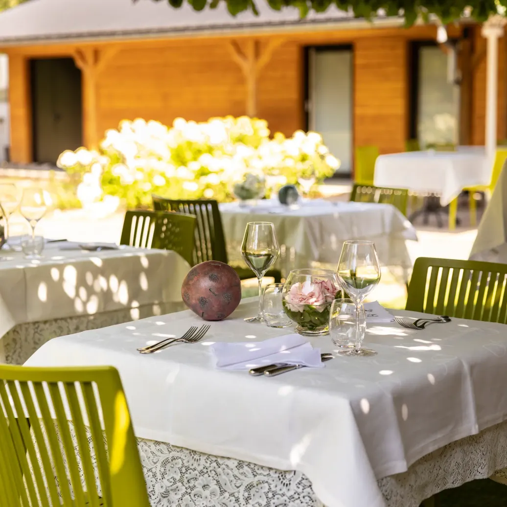 Tables en extérieur avec nappes blanches, verres à vin, couverts et décoration florale sous un auvent en bois