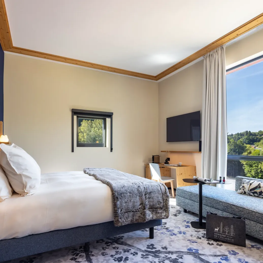 Chambre avec un lit, une table de chevet, un canapé et une grande fenêtre offrant une vue sur une forêt
