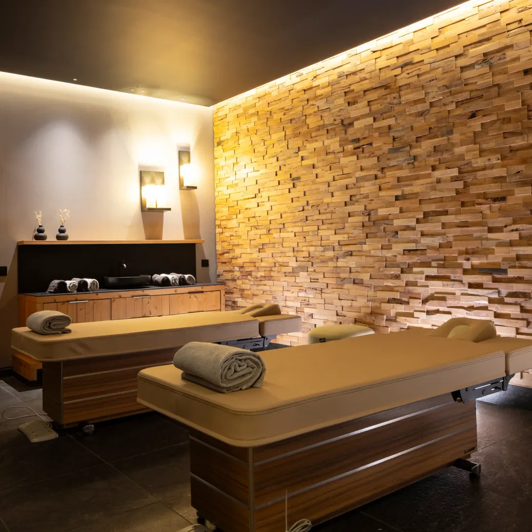 Salle de massage avec deux tables de massage, une paroi en briques apparentes et des serviettes roulées