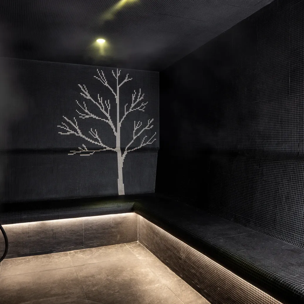 Mur de douche noir avec une mosaïque de petits carreaux représentant un arbre stylisé en blanc, éclairé par une lumière douce au plafond