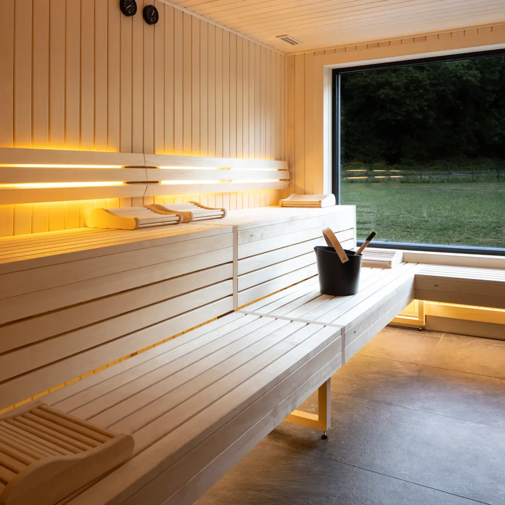 Salle de sauna en bois avec des bancs, une fenêtre donnant sur un paysage extérieur et un seau avec des accessoires