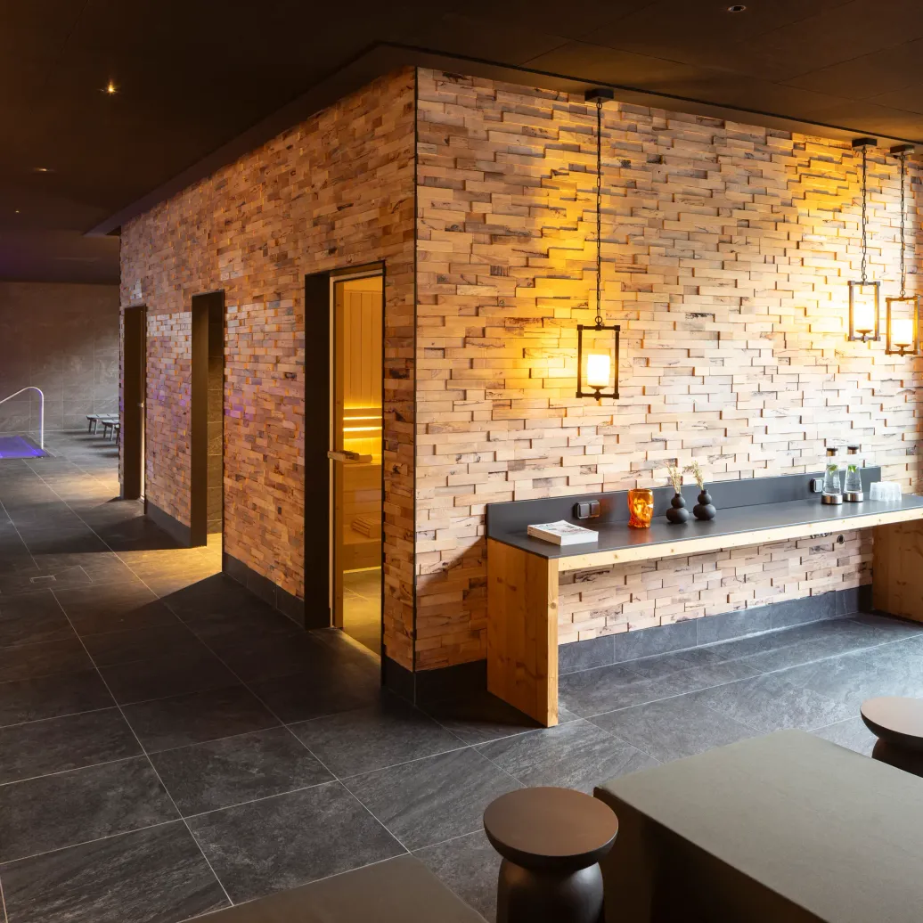 Intérieur moderne avec un mur en briques éclairé, un comptoir en bois et des portes ouvertes menant à une pièce faiblement éclairée