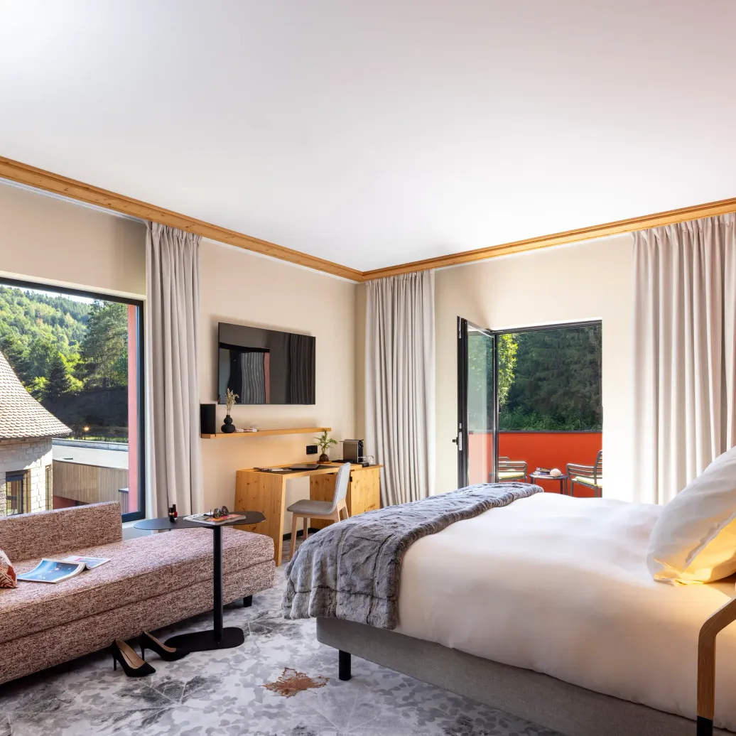 Chambre lumineuse avec lit, canapé, bureau et vue sur des toits traditionnels et une forêt