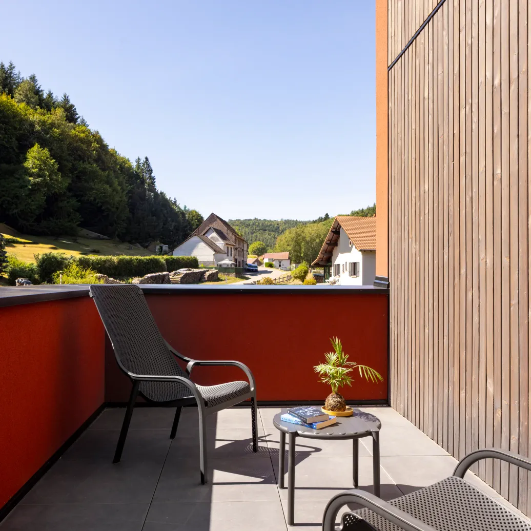 Balcon avec trois chaises et une table basse, vue sur des maisons et des collines boisées