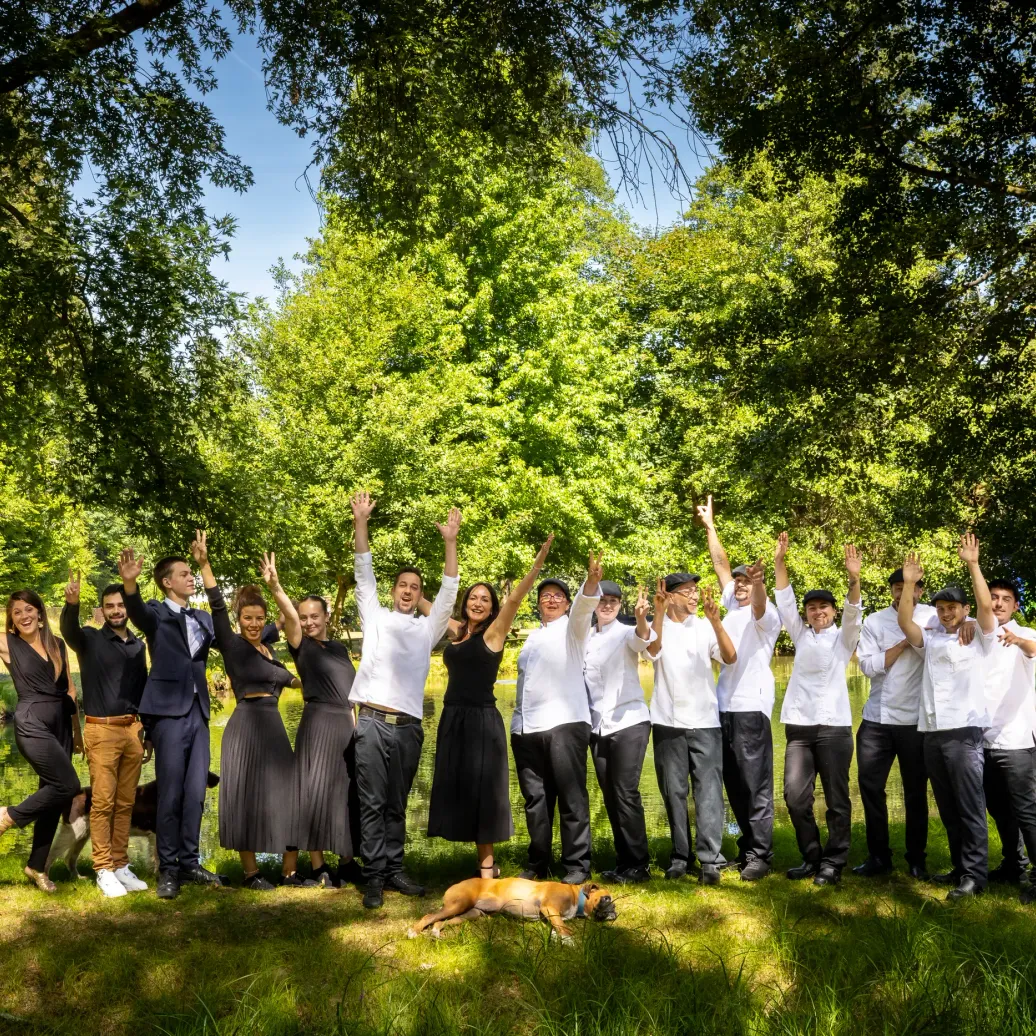 Un groupe de personnes lève les bras en l'air dans un parc arboré près d'un plan d'eau