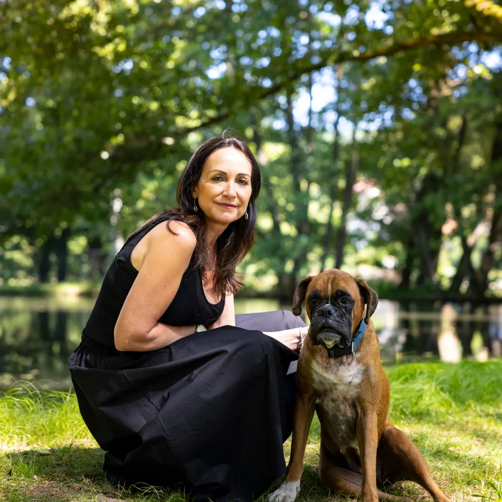 Femme en robe noire assise dans l'herbe avec un chien boxer à côté d'elle dans un parc arboré