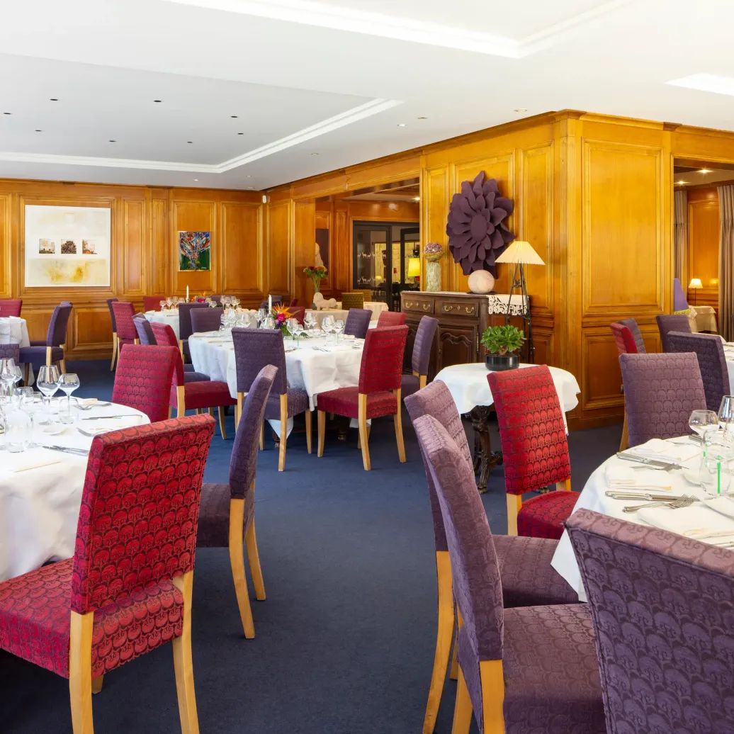 Salle de restaurant élégante avec tables dressées, nappes blanches, chaises rembourrées et décor floral