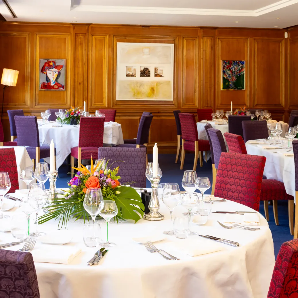 Une salle à manger élégante avec des tables dressées, des chandeliers, des verres et des fleurs au centre des tables