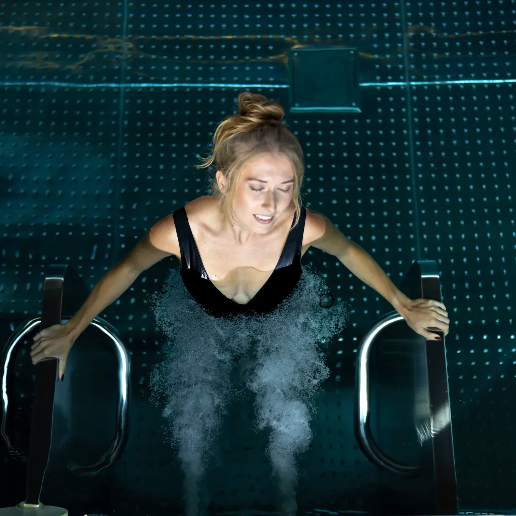 Une femme en tenue de sport fait de l'exercice dans une piscine avec des jets d'eau visibles autour d'elle