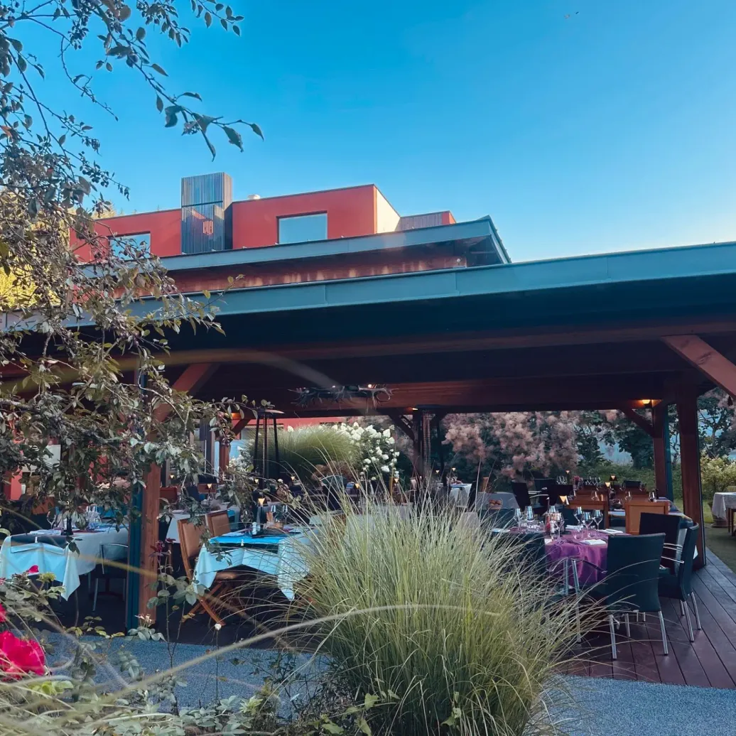 Une terrasse couverte avec des tables dressées pour un repas, entourée de végétation et de fleurs, sous un ciel dégagé