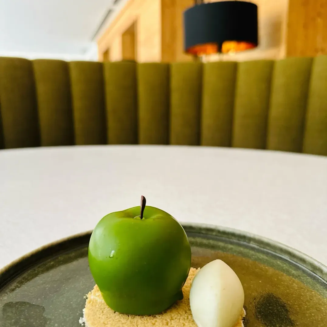Un dessert composé d'une pomme verte et d'une boule de glace blanche sur un lit de crumble, présenté sur une assiette verte