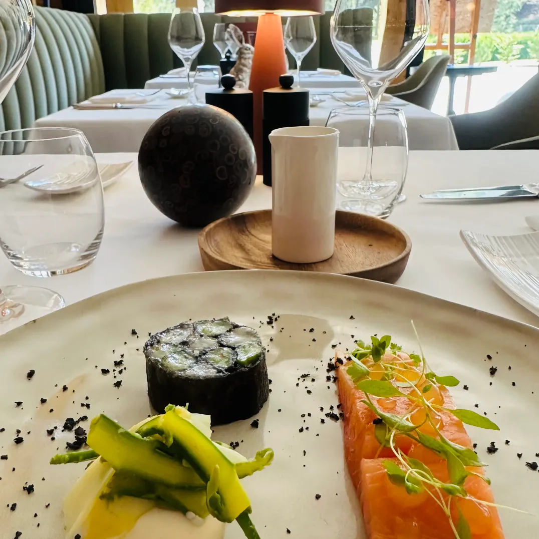 Assiette de plats fins avec sushi, saumon et légumes, posée sur une table élégante avec verres à vin et décoration