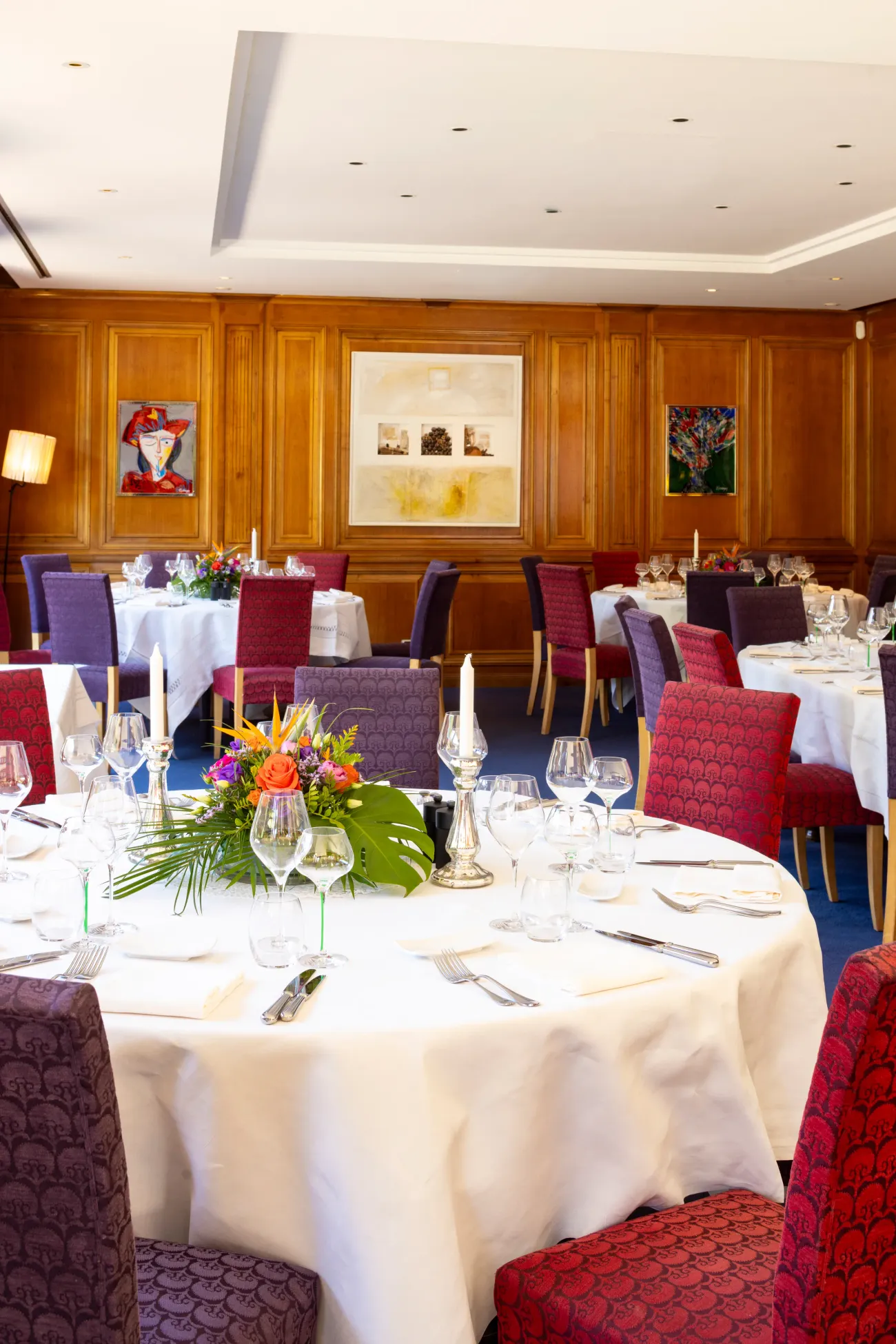 Une salle à manger élégante avec des tables dressées, des chandeliers, des verres et des fleurs au centre des tables