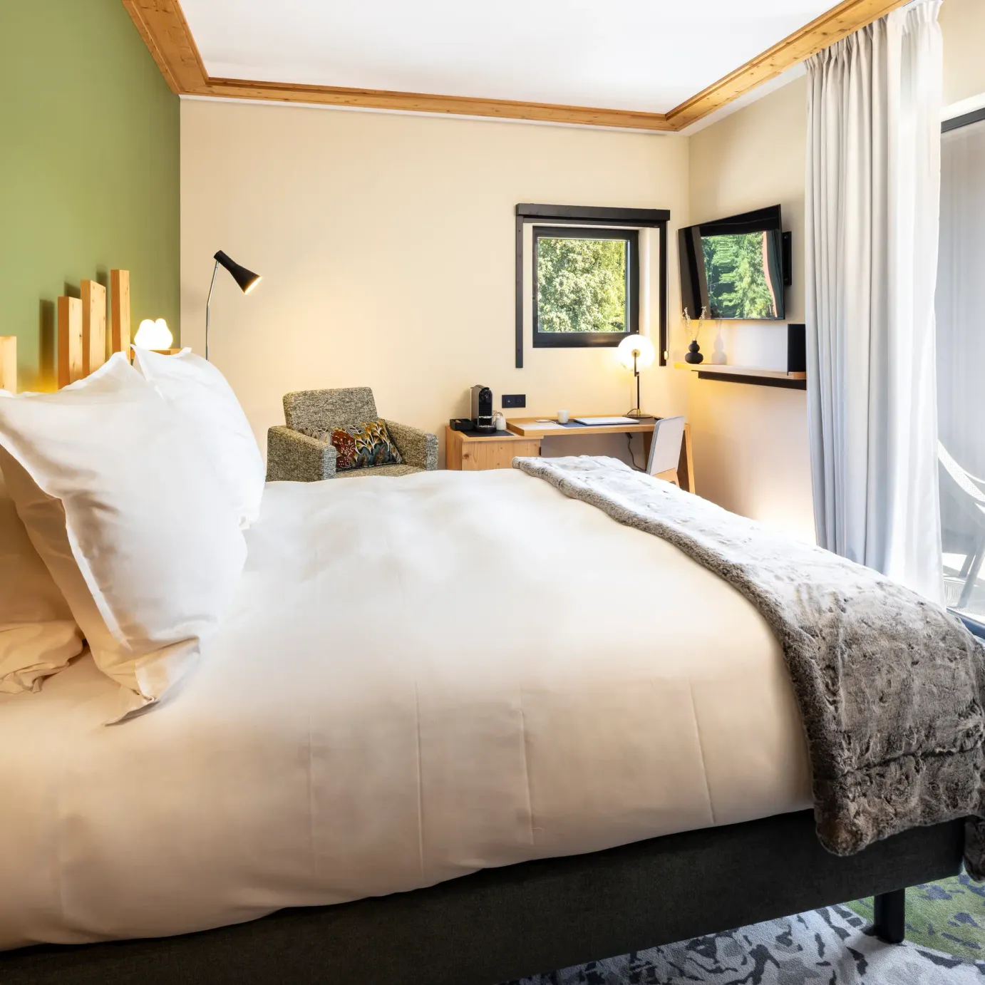 Chambre avec un lit double, une table de chevet, un bureau, des fenêtres avec vue sur l'extérieur et une porte vitrée donnant sur un balcon