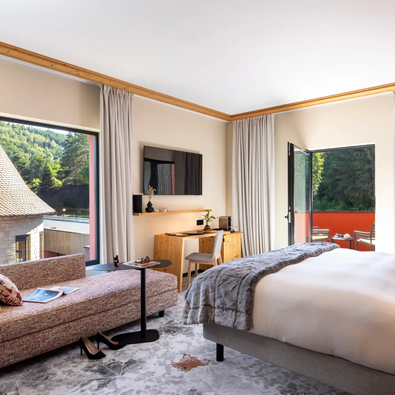 Chambre avec lit, canapé, bureau et vue sur des toits traditionnels et une forêt