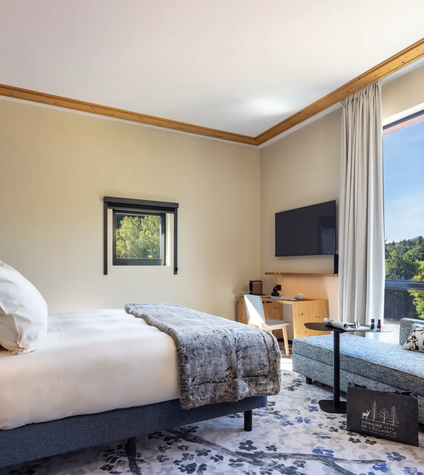 Chambre avec un lit, une table de chevet, un canapé et une grande fenêtre offrant une vue sur une forêt