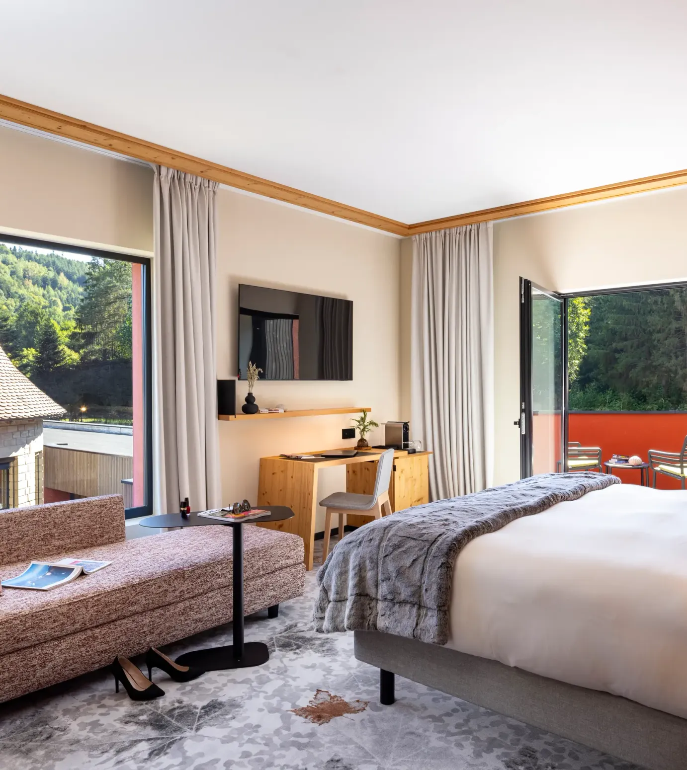 Chambre avec lit, canapé, bureau et vue sur des toits traditionnels et une forêt