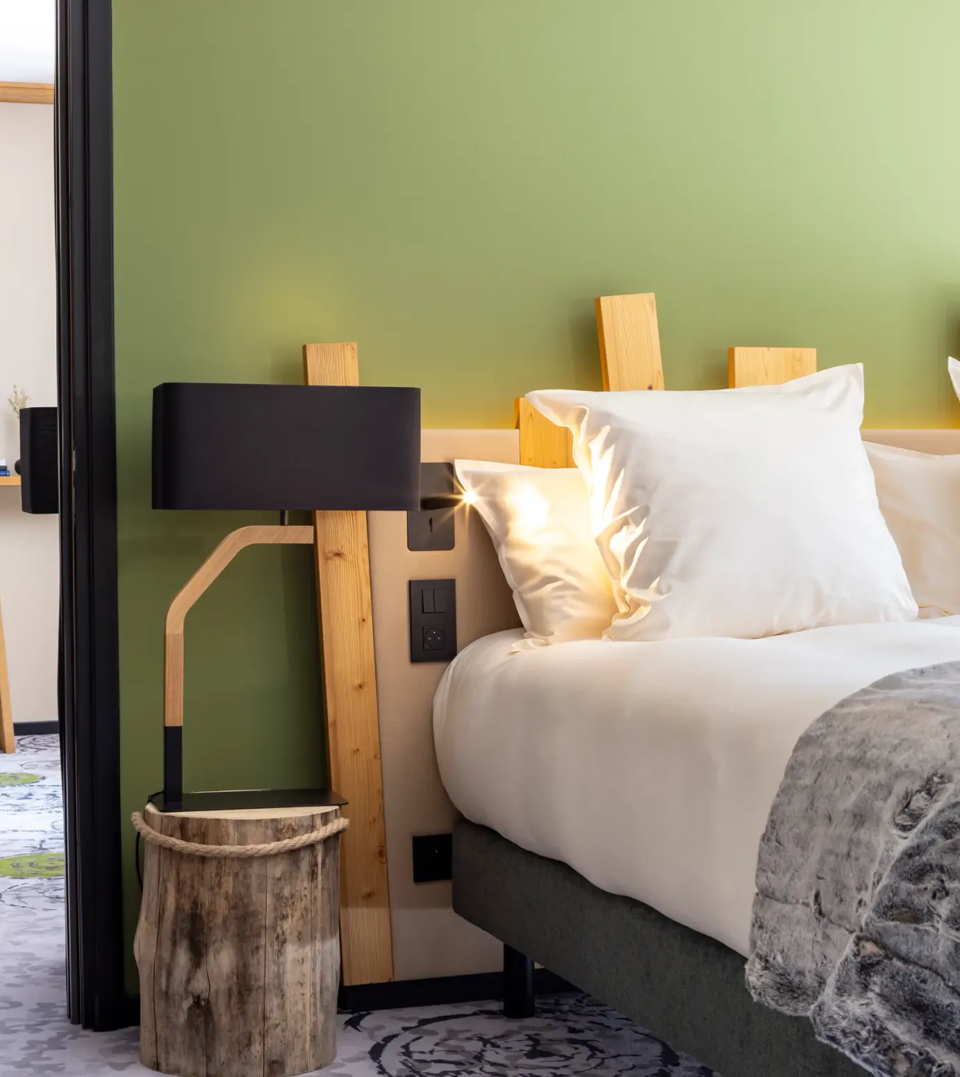 Hotel room with a double bed, a wooden bedside lamp, a television, and a desk with a chair.
