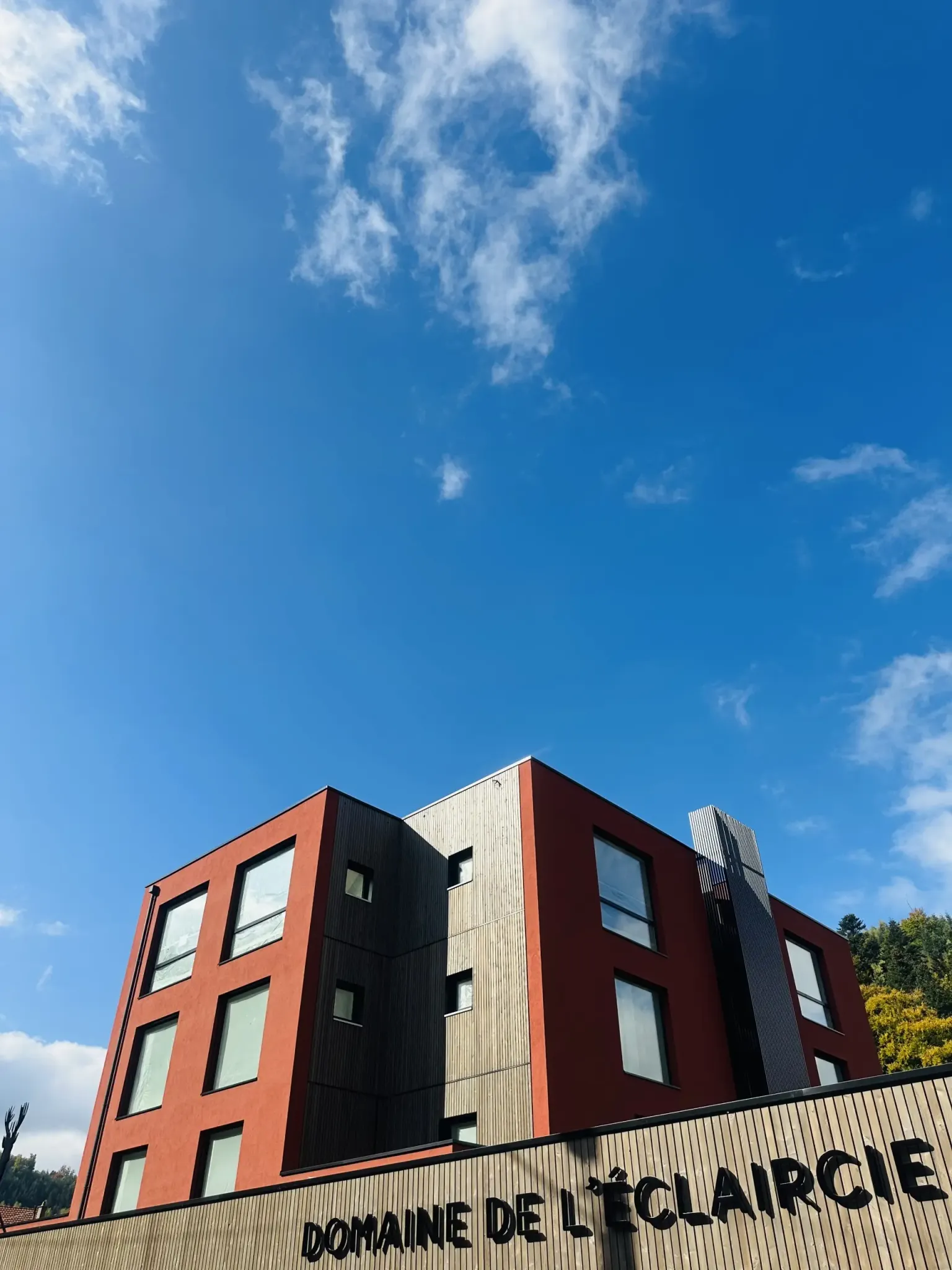 Bâtiment moderne en briques rouges et noires avec le nom "Domaine de l'Éclaircie" affiché sur la façade sous un ciel bleu avec quelques nuages
