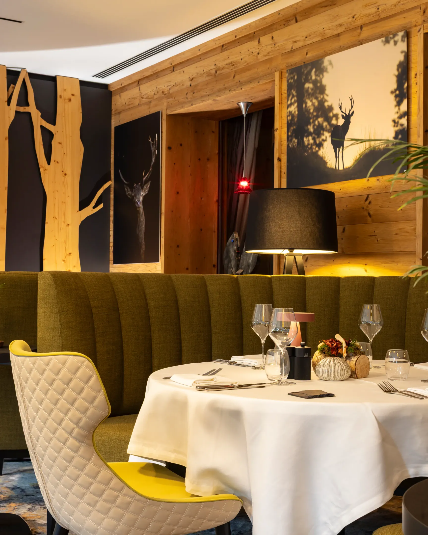 Table dressée avec verres et couverts dans un restaurant à la décoration bois et vert, avec des chandeliers et des œuvres murales