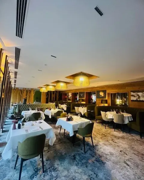 Restaurant élégant avec plusieurs tables couvertes de nappes blanches, des chaises vertes et des luminaires suspendus au plafond
