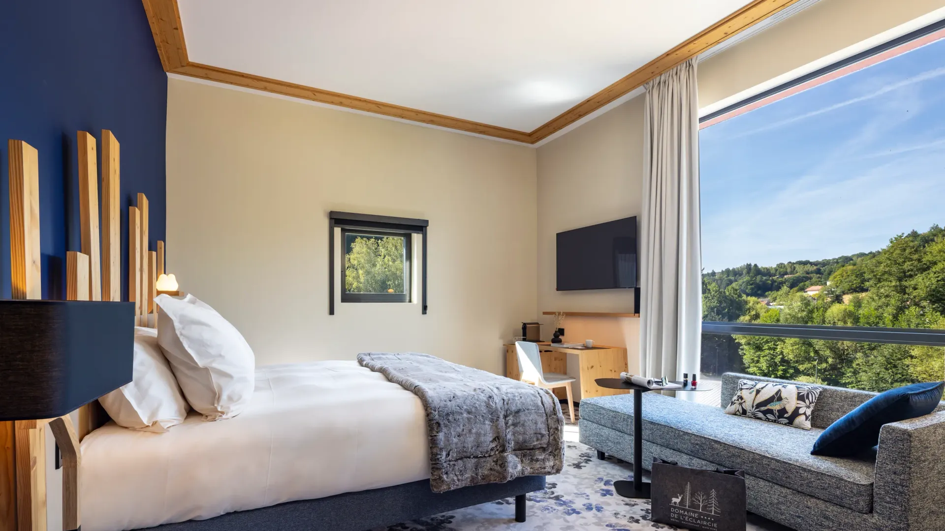 Chambre avec un lit, une table de chevet, un canapé et une grande fenêtre offrant une vue sur une forêt