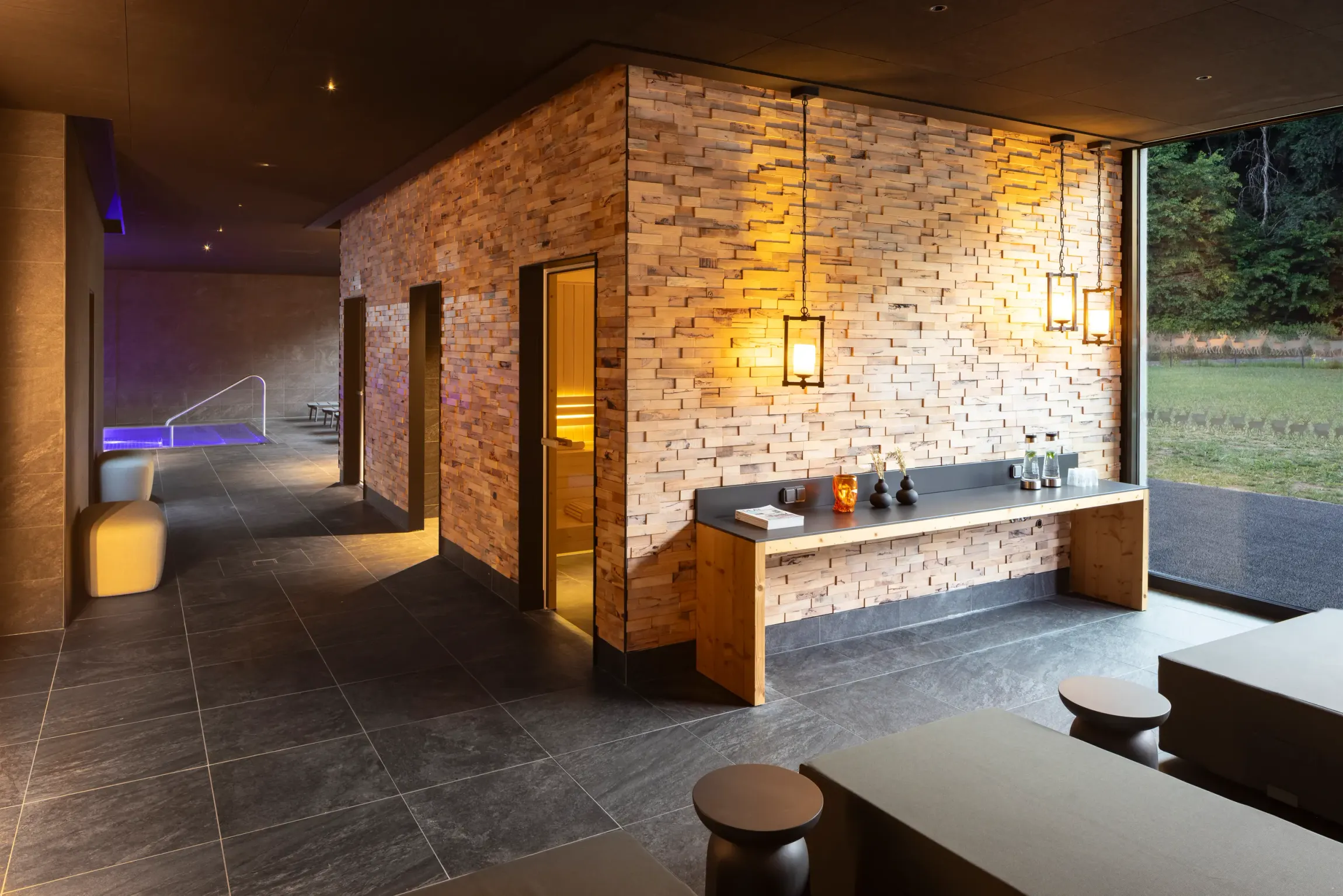 Intérieur moderne avec un mur en briques éclairé, un comptoir en bois et des portes ouvertes menant à une pièce faiblement éclairée