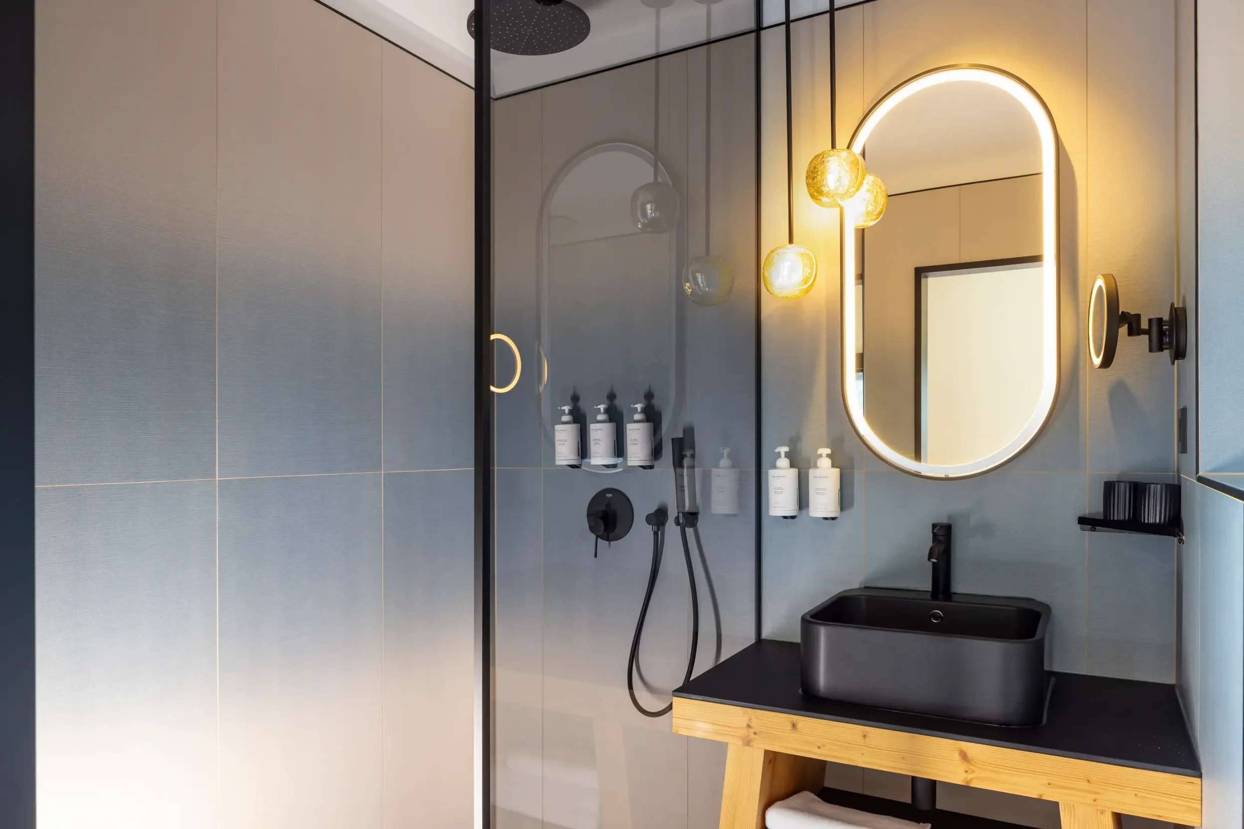 Salle de bain moderne avec miroir ovale, lavabo noir sur meuble en bois et produits de toilette alignés