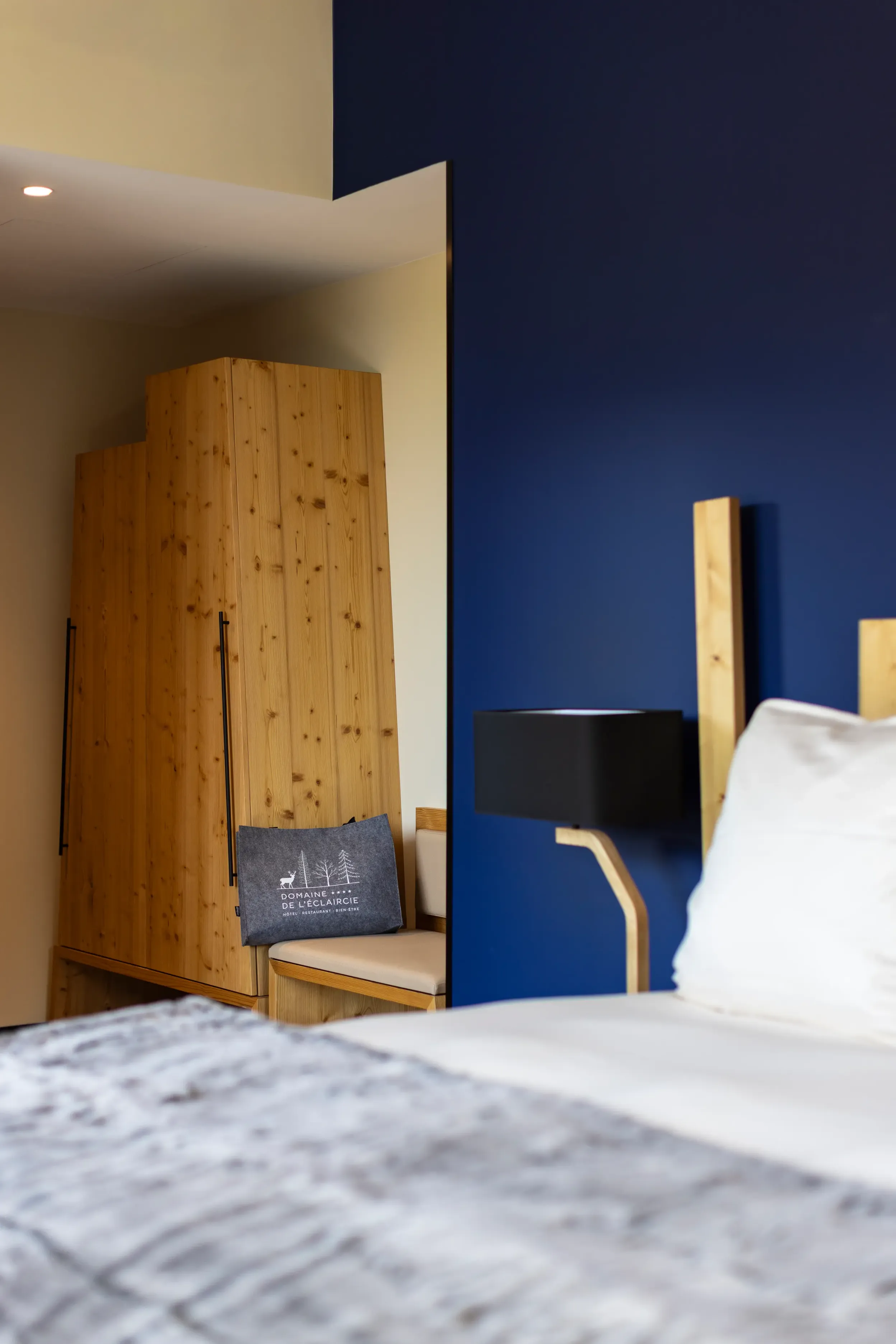 Chambre avec lit, tête de lit en bois, murs peints en bleu et beige, et coussin avec texte et logo