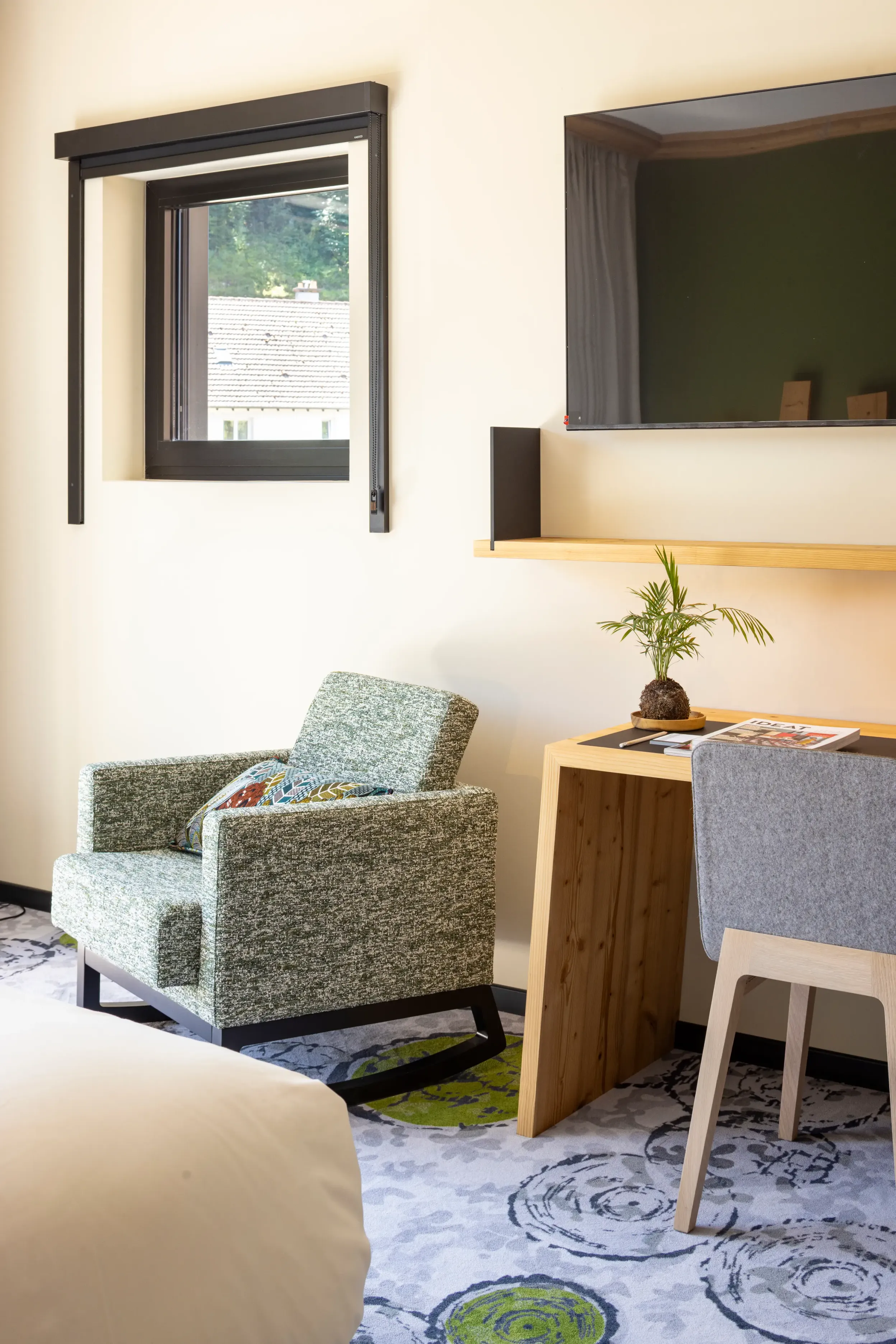 Un fauteuil vert et un bureau en bois clair dans une pièce avec une fenêtre et une télévision