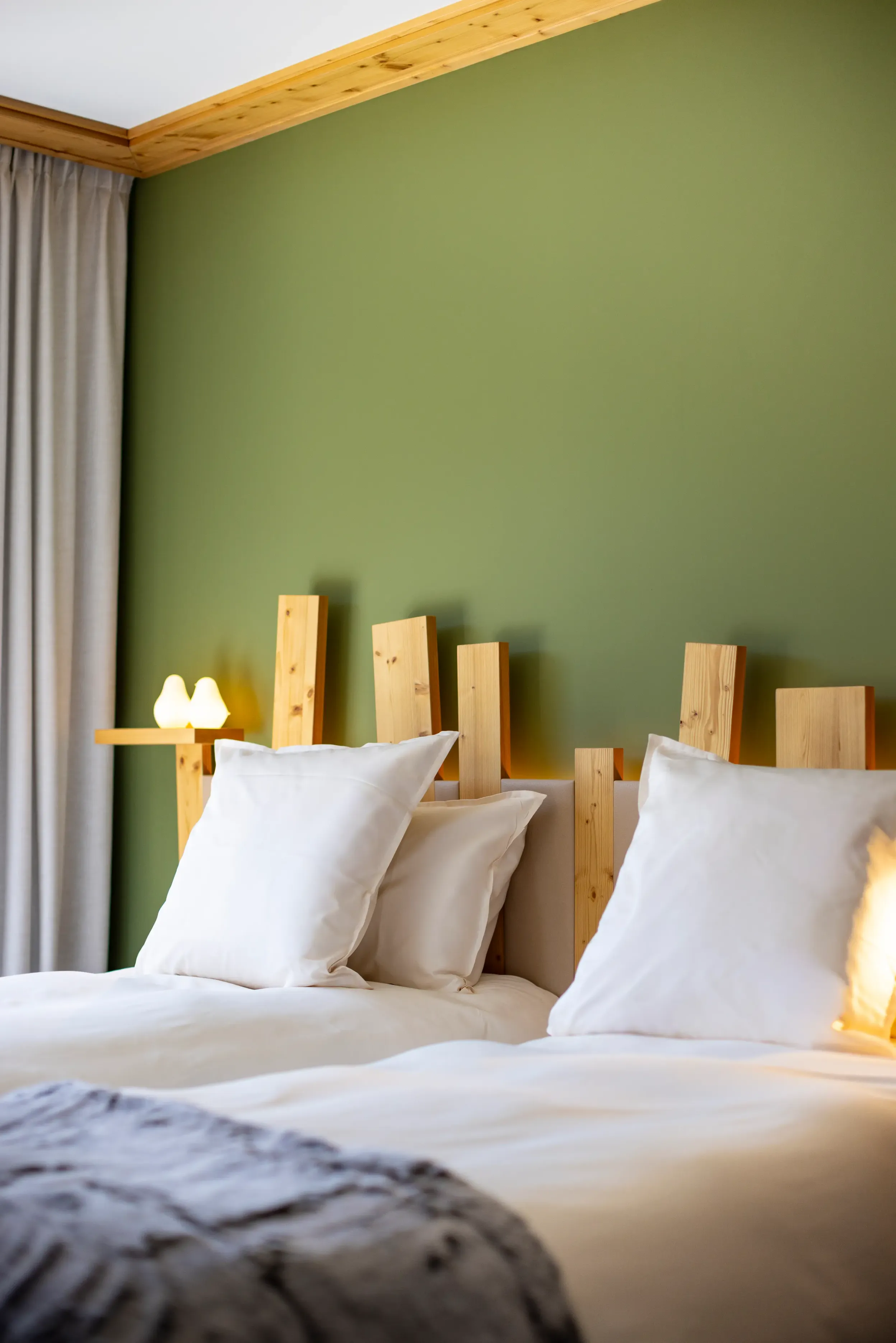 Lit avec une tête de lit en bois et des oreillers blancs, dans une chambre à la peinture murale verte