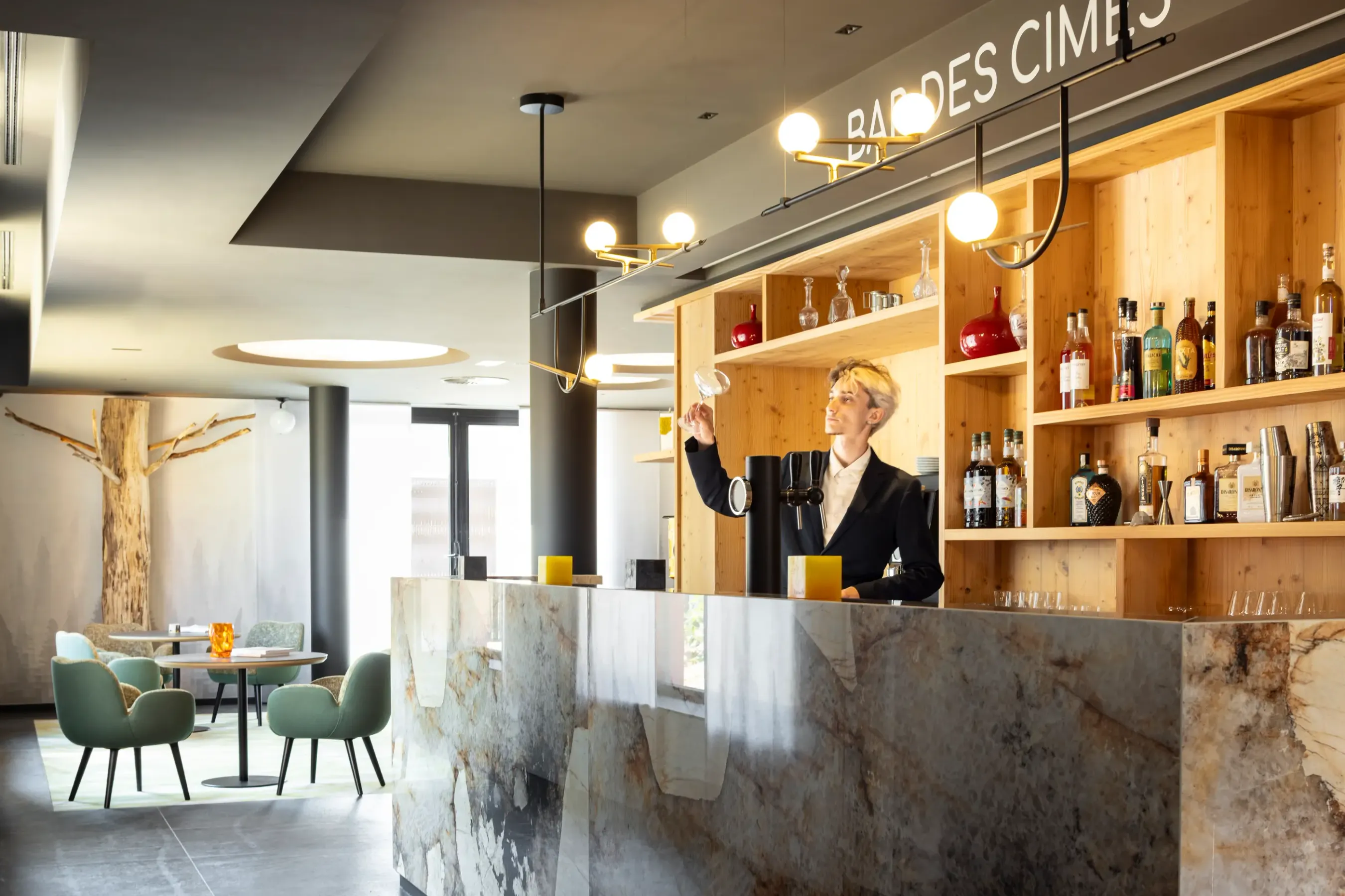 Un barman prépare un verre derrière un comptoir en marbre, avec des étagères en bois remplies de bouteilles derrière lui.