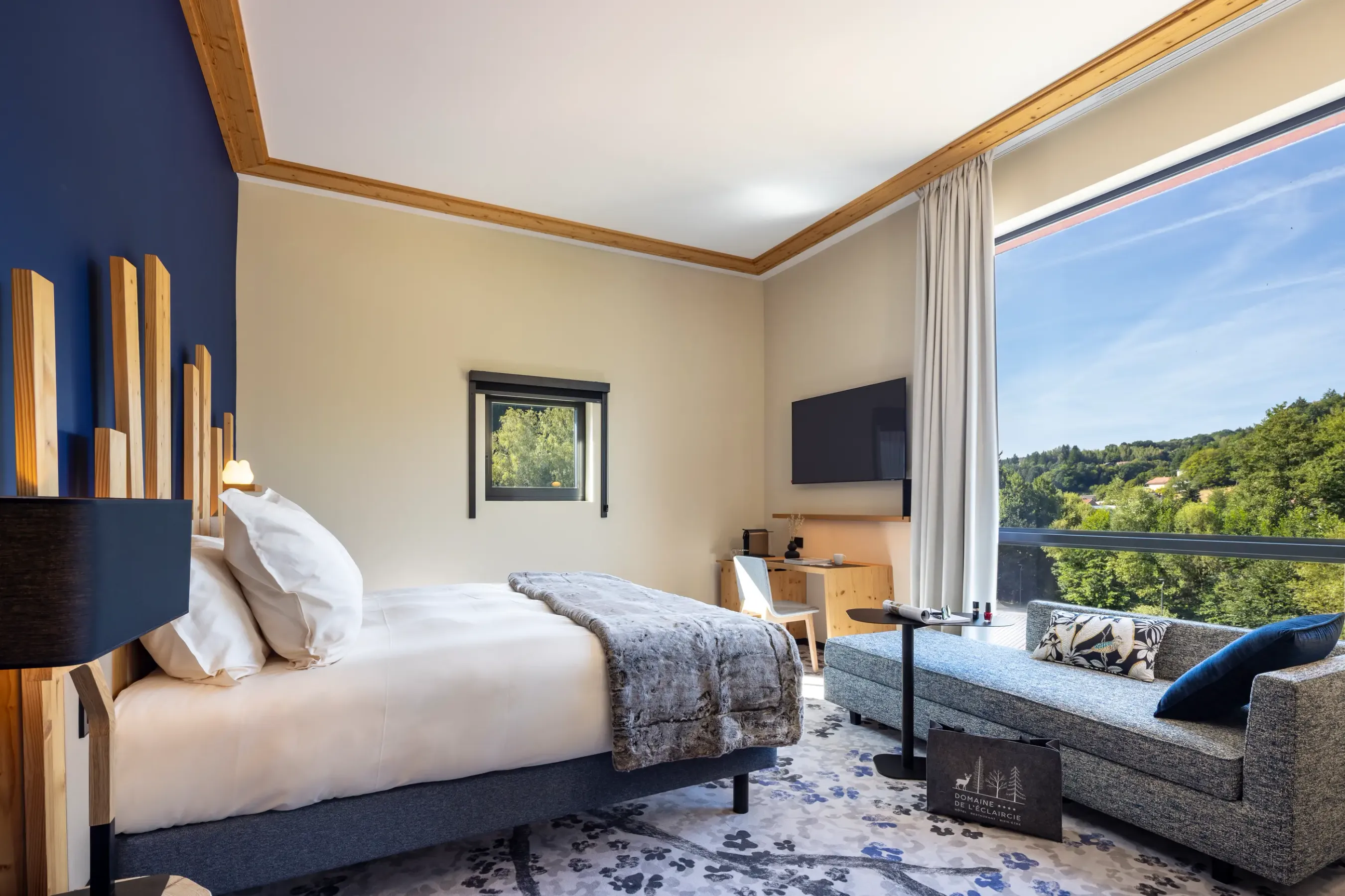 Chambre avec un lit, une table de chevet, un canapé et une grande fenêtre offrant une vue sur une forêt