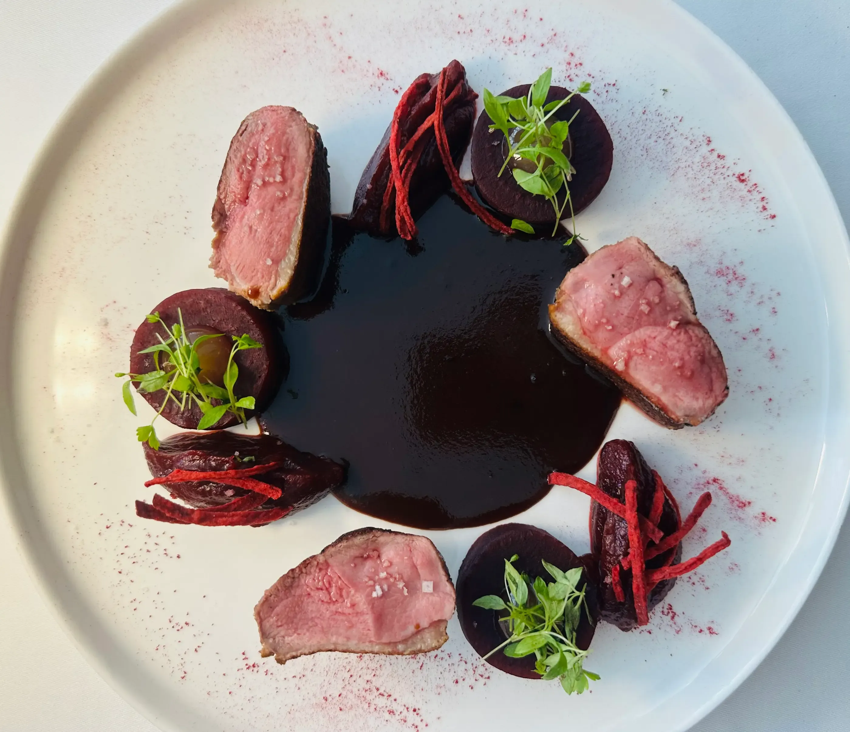 Assiette avec des tranches de viande, des rondelles de betterave garnies de micro-pousses et une sauce au centre