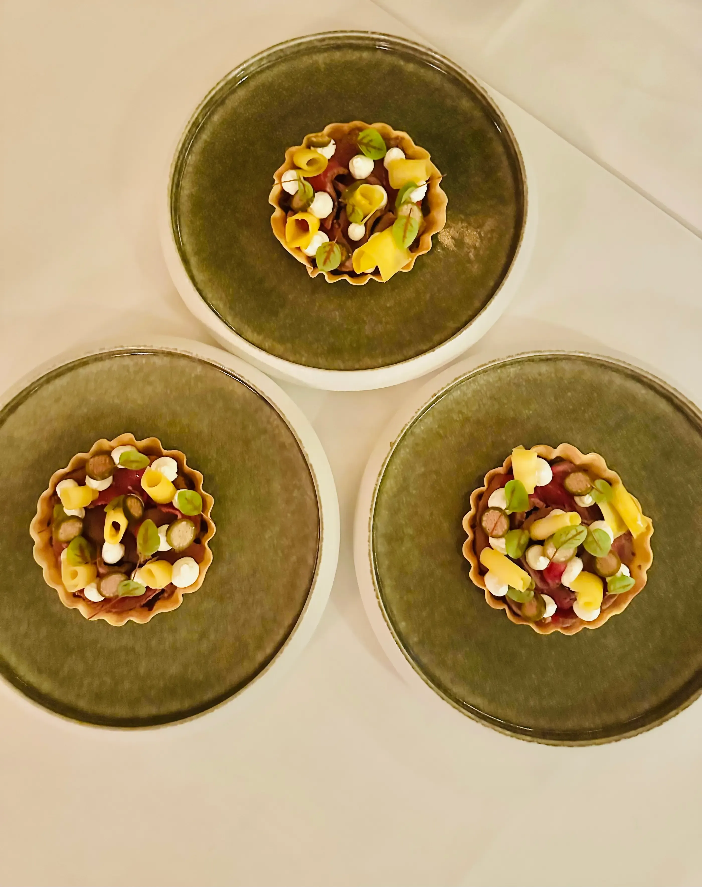 Trois tartelettes garnies de divers ingrédients sur des assiettes vert foncé