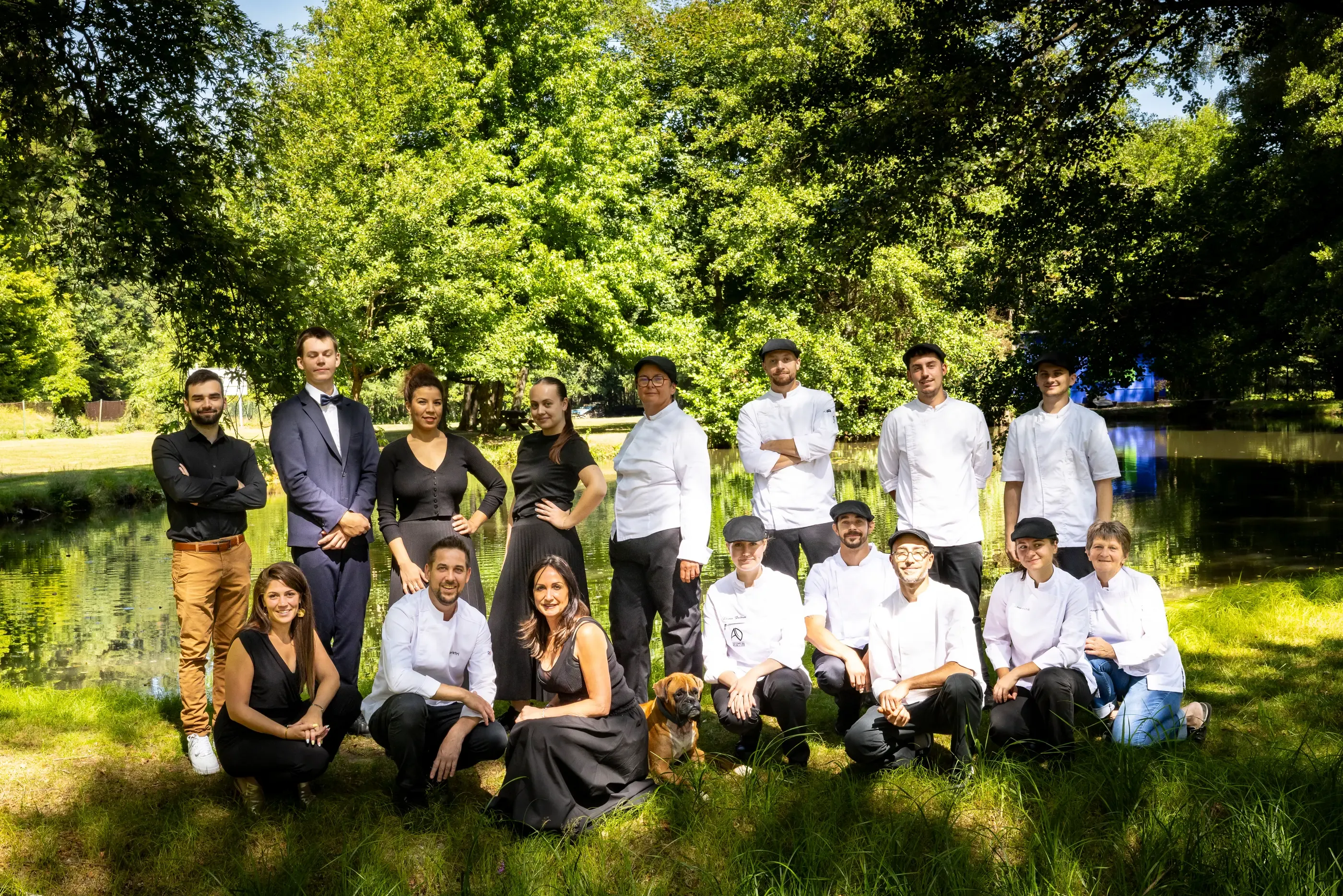 A group of people in professional attire pose in front of a body of water surrounded by trees.