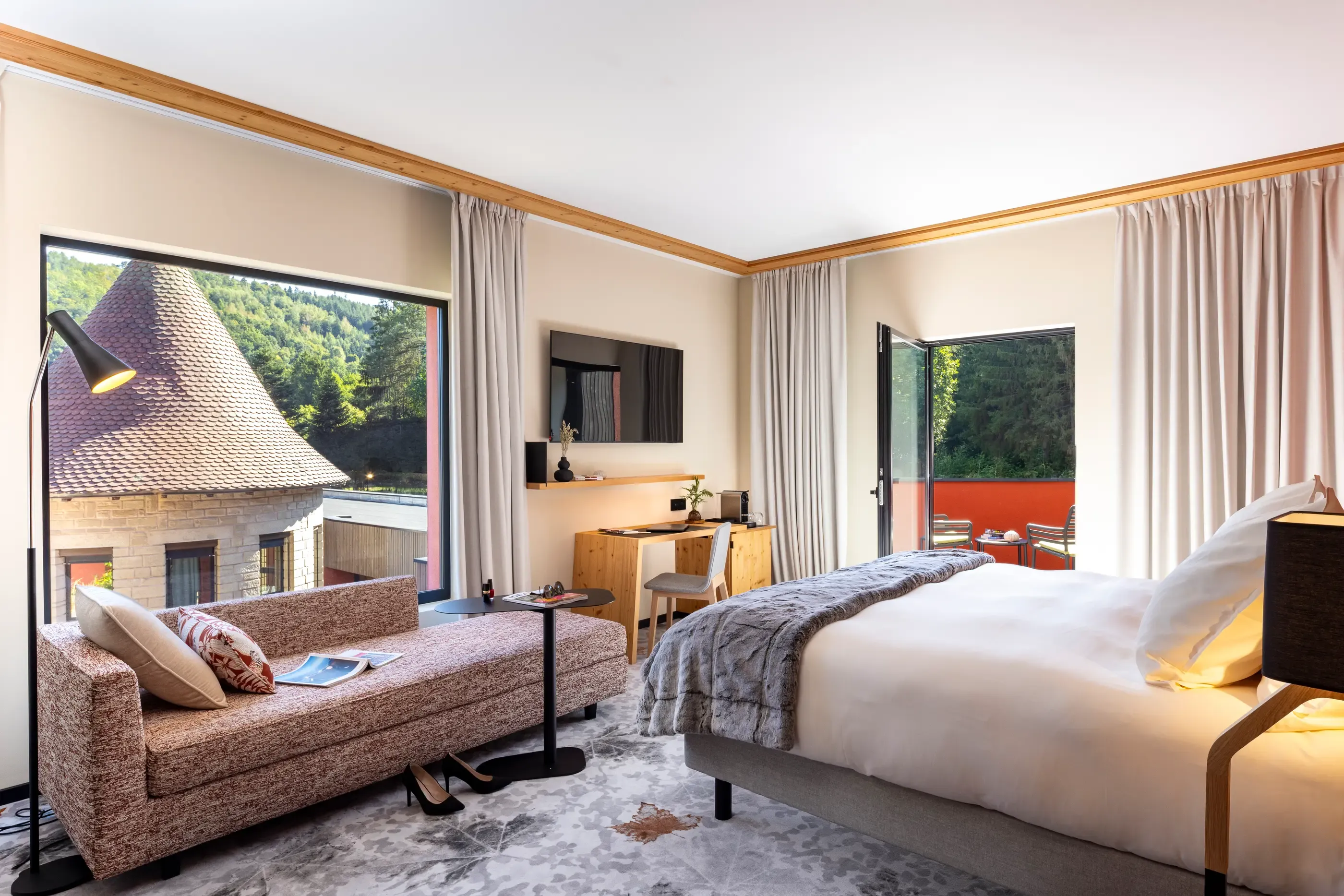 Room with bed, sofa, desk and view of traditional rooftops and a forest