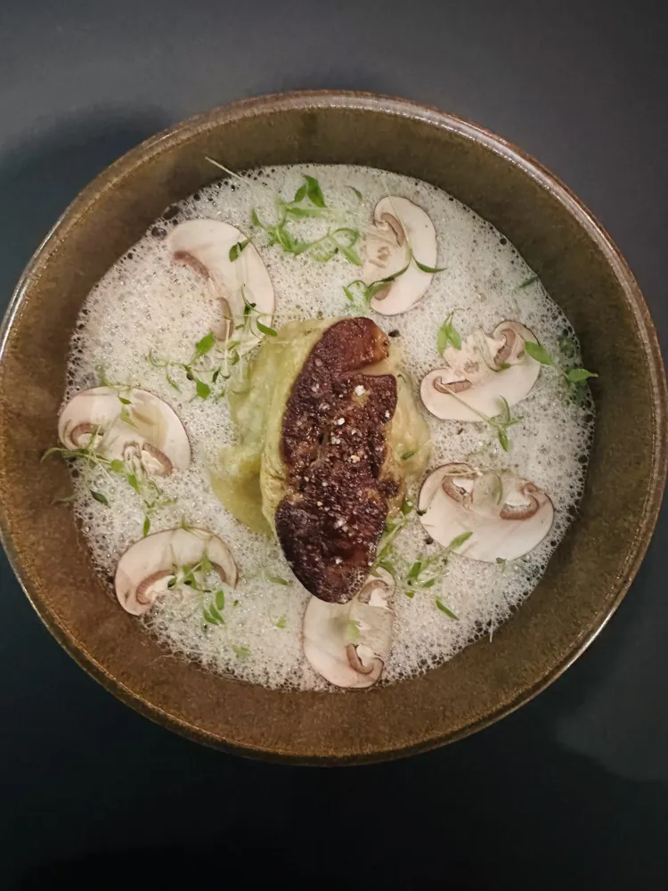 Un bol contenant une soupe avec des tranches de champignons, des pousses et un morceau de truffe noire