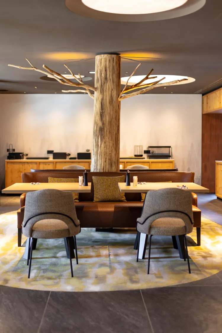 Un espace intérieur avec une table entourée de chaises et d'un canapé, un arbre central décoré de branches lumineuses et un comptoir en arrière-plan