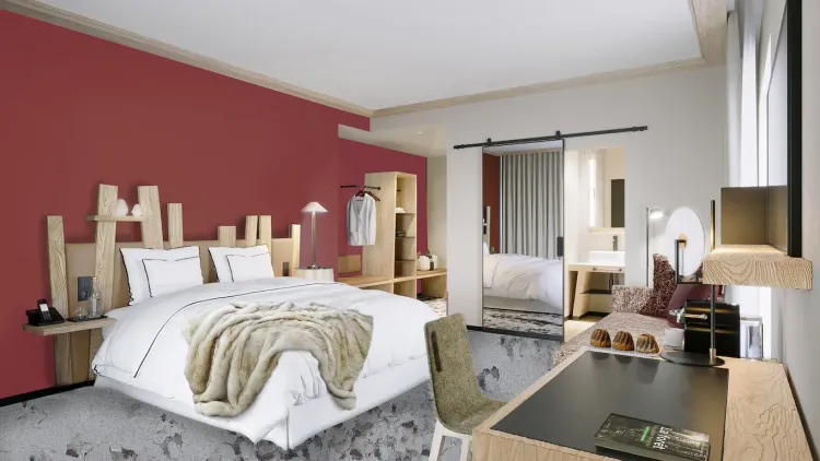 Chambre moderne avec un lit blanc et une couverture en fourrure, des meubles en bois clair, un bureau avec des pâtisseries et une porte ouverte sur une salle de bain