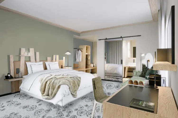 Chambre moderne avec un grand lit blanc, une couverture beige, des tables de chevet en bois, un coin bureau et un dressing visible à travers une porte ouverte