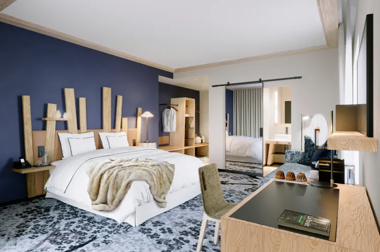 Chambre moderne avec un lit double, une table de chevet, un bureau et une armoire visible à travers une porte ouverte