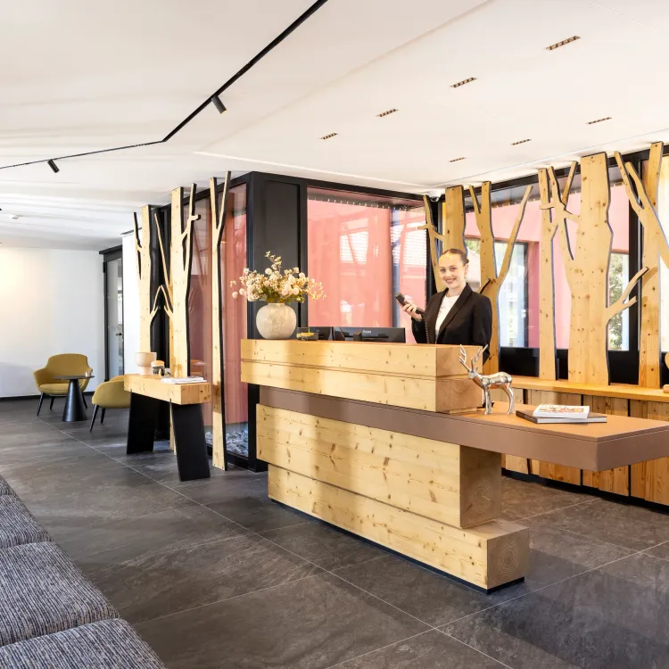 Réception moderne avec un comptoir en bois, une personne derrière le comptoir et des chaises autour de tables basses