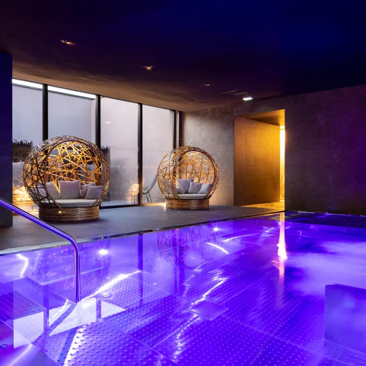 Piscine intérieure éclairée en violet avec des sphères en osier servant de sièges dans un espace moderne aux murs sombres
