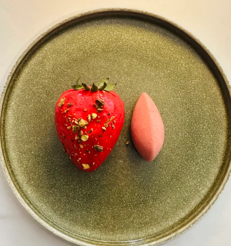 Une fraise décorée et un objet rose allongé sur une assiette verte